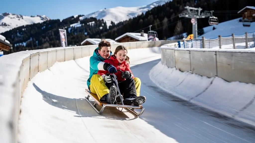 Deux adolescents sur une luge bi-place descendant une piste de luge aménagée à La Plagne, vêtements d'hiver colorés, activité hors-ski