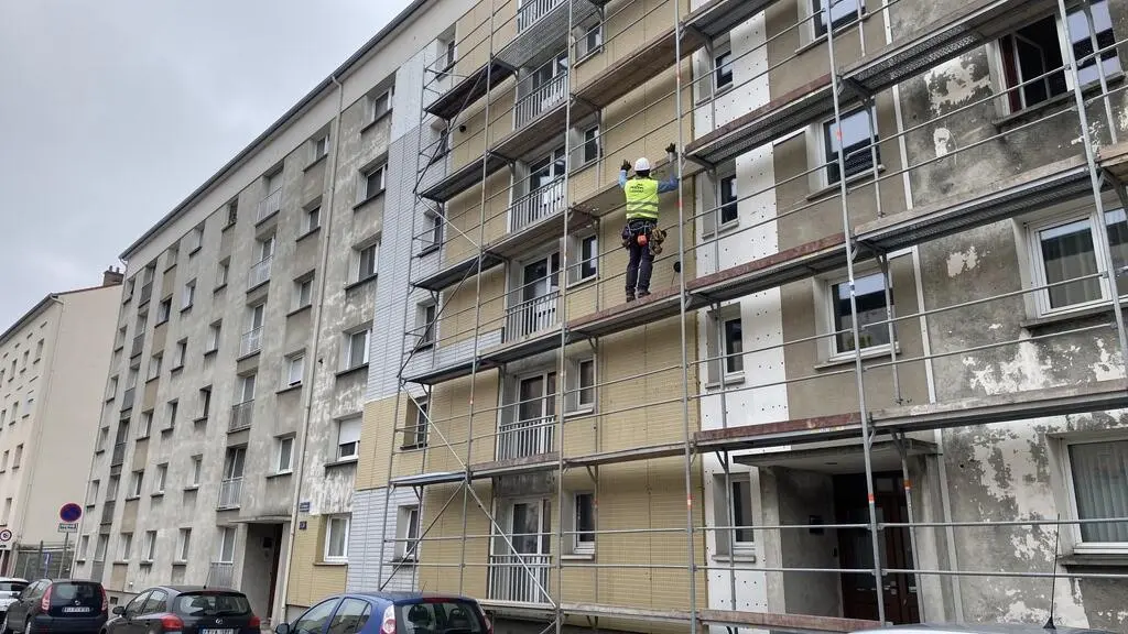 Ouvrier installant une isolation thermique par l'extérieur sur la façade d'un immeuble résidentiel français des années 1960.